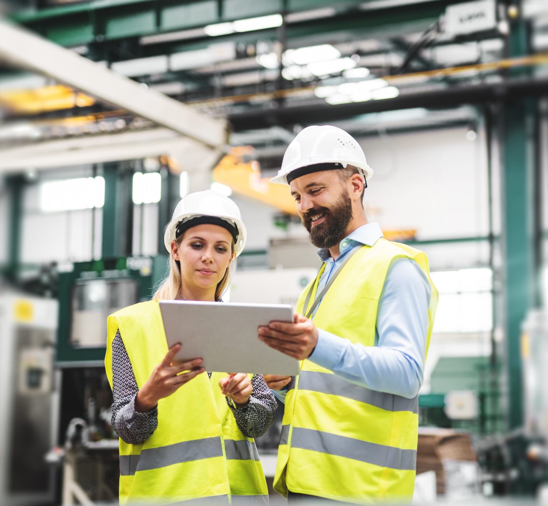 A portrait of a mature industrial man and woman engineer with tablet in a factory, talking.